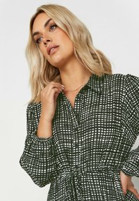 Svartvit mönstrad skjortklänning med krage, långa ärmar, insydd midja och knappstängning, med ett rutmönster och mjuk textur.