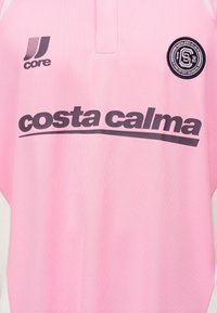 Maillot de sport rose avec le texte « costa calma », logo Core sur le côté gauche de la poitrine et écusson du club athlétique rond sur le côté droit de la poitrine.