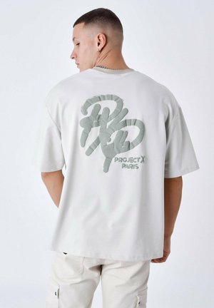 Camiseta de color gris claro que presenta un gráfico texturizado en verde de "Project X Paris" en la parte posterior. Diseño de mangas cortas y corte relajado.