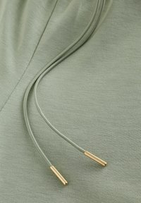 Tissu vert clair avec deux cordons assortis se terminant par des embouts métalliques dorés, étalés à plat.