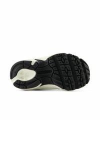 Semelle à crampons noire et blanche d'une chaussure de sport New Balance, montrant un motif de grip détaillé et le logo de la marque au centre.