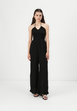 Black halter jumpsuit with a smocked bodice, loose wide-leg design, and thin straps. The fabric is lightweight and flowing.