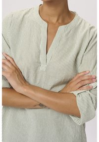 Striped, light green tunic with a mandarin collar, short sleeves rolled up, button detail near cuffs, and textured fabric.