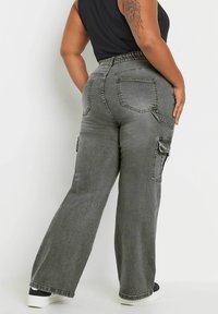 Pantalones cargo de pierna ancha en gris con cinturilla elástica, bolsillos laterales y bolsillos traseros. La tela tiene un acabado suave y texturizado.