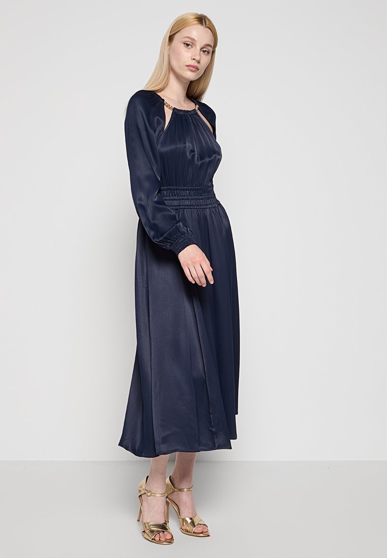 Abito in satin navy con maniche lunghe, vita smock e dettagli in hardware dorato. Presenta una gonna fluida lunga fino alla caviglia e una vestibilità rilassata.