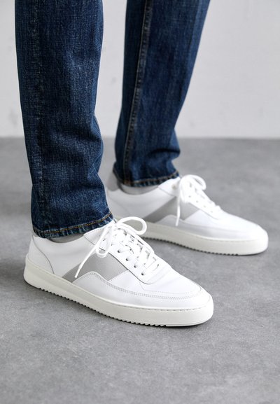 Sneakers albe din piele și materiale sintetice, cu un accent gri texturat, vârf rotund și talpă plată din cauciuc. Asortați cu blugi albaștri.