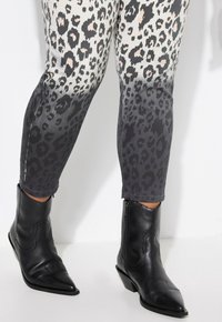 Jeans skinny in denim con stampa leopardata che sfumano dal crema al grigio, abbinati a stivaletti neri in pelle con punta e cerniera laterale.