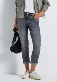 Jeans en denim gris avec une coupe décontractée, finitions roulées et détails de décoloration subtils, associés à des baskets blanches et un sac à épaule noir.