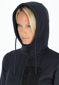 Navy hooded sweatshirt with a high collar, featuring a black zippered pocket and drawstrings, smooth texture, and close-fitting design.