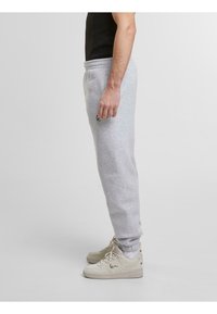 Grijze sweatpants met een taps toelopend ontwerp, gemaakt van zacht materiaal. Heeft een elastische tailleband en een klein zwart logo aan de zijkant. Gecombineerd met beige sneakers.