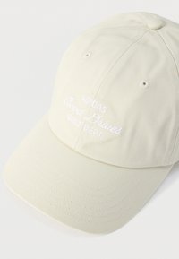 Μπεζ καπέλο μπέιζμπολ με λευκά κεντημένα γράμματα "ADIDAS Good Grives GOLF DEPT" στην μπροστινή πλευρά.