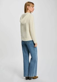 Felpa soffice color crema con coulisse e spacco posteriore; abbinata a jeans a vita alta in denim azzurro chiaro con gamba larga e stivali piattaforma marroni.