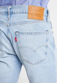 Světle modré džíny mají klasický design s koženou nášivkou, červeným štítkem a dvěma zadními kapsami s detaily šití.
