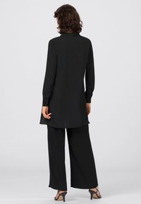 Mustat pitkähihaiset tunikat, jossa on hieman levenevä helma, ja yhdistelemättömät leveälahkeiset housut. Silkkinen kangas ja avonainen selkädesign. Korotetut sandaalit.