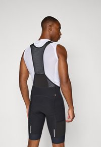 Svarte sykkel bib-shorts med nettstropper, som har polstret sete, reflekterende detaljer og strømlinjeformet design for ytelse.