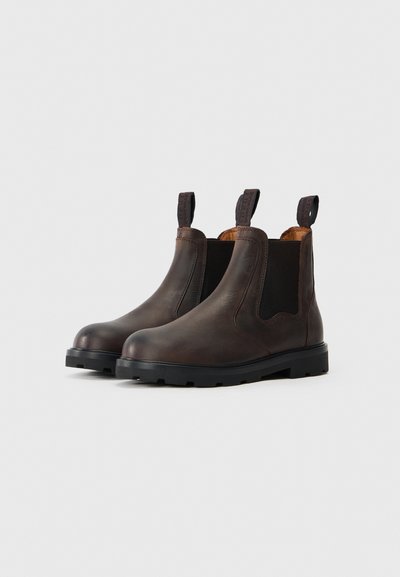 Botas Chelsea em couro castanho com painéis elásticos laterais, alças de puxar e solas de borracha texturizada. Bico arredondado e design minimalista.