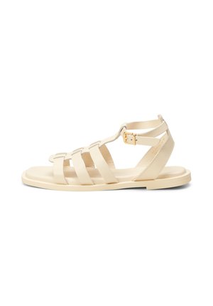 Sandales en cuir beige avec plusieurs sangles horizontales, fermeture à boucle à la cheville, semelle plate et design minimaliste. Texture lisse et forme moderne.