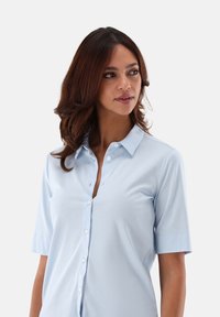 Light blue button-up shirt with a collar, short sleeves, and a smooth, soft texture. Notable for its simple design and four buttons along the front.