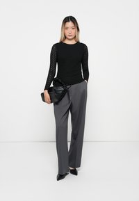 Black lace long-sleeve top with a textured pattern, paired with gray high-waisted trousers and a black clutch-like bag. Black pointed toe heels.