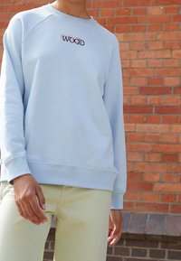 Sudadera azul claro con cuello redondo acanalado y mangas raglán, con la palabra "WOOD" bordada en hilo oscuro en el pecho.
