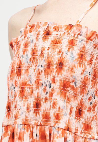 Φόρεμα χωρίς τιράντες με μοτίβο tie-dye σε πορτοκαλί, λευκό και μαύρο, με φουσκωτό μπούστο και λεπτές τιράντες στους ώμους στο πάνω μέρος του κορμού ενός ατόμου.