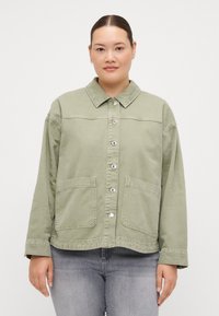 Green denim jacket with a button-up front, pointed collar, and two front pockets. Features a relaxed fit and visible stitching details.