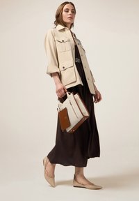 Beige Baumwolljacke mit Knopfverschluss, langes braunes Kleid, beige Ballerinas mit Kettendetails und eine strukturierte Handtasche mit Lederakzenten.