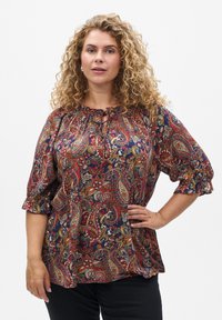Bluza u crvenoj i mornarskoj plavoj boji s uzorkom paisley, s nabranim izrezom, kratkim napuhanim rukavima i teksturiranim materijalom, koja sadrži cvjetne i paisley uzorke.