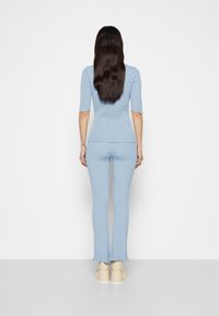 Ensemble deux pièces bleu clair à côtes comprenant un haut ajusté à manches courtes et un pantalon évasé, tous deux avec des détails d'ourlet effilochés.