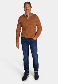 Oranje gebreide trui met een ritskraag, gecombineerd met donkere jeans en zwarte sneakers, met een gestructureerde stof en een aansluitend ontwerp.