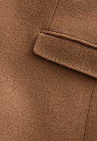 Bruine wollen stof met een gladde textuur, voorzien van een zichtbare bieszak en nauwkeurige stikdetails langs de randen.