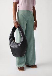 Fekete bőr hobo táska ívelt siluettel, zipzáros záródással és diszkrét varrási részletekkel, zöld kordbársony nadrággal párosítva.