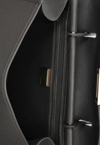 Grijze leren handtas met een gestructureerde afwerking, voorzien van een ritszak en gouden hardware, met zicht op het interieurontwerp en de stikdetails.