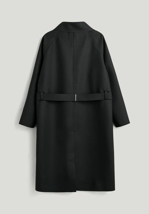 Sort lang frakke med bæltebagdetalje, lange ærmer og lige kant, vist bagfra mod en ensartet lys baggrund.