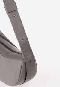 Borsa a spalla grigia in pelle con tracolla regolabile e cerniera nera su sfondo bianco.