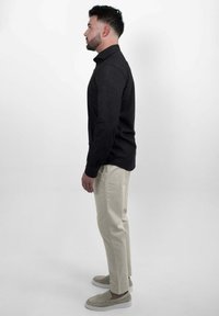 Zwarte lange mouwen shirt gecombineerd met beige slim-fit broeken en lichtgrijze instappers. Schone lijnen, minimalistisch ontwerp en neutrale kleuren.