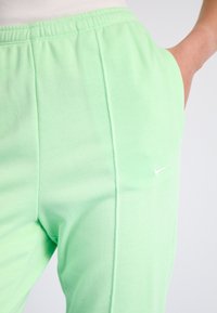 Närbild av en person som bär ljusgröna Nike-träningsbyxor med elastisk midja, hand placerad i den högra fickan.