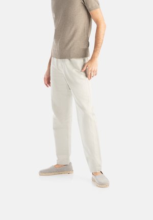 Pull en tricot gris, pantalon loose de couleur claire et espadrilles grises avec des semelles en jute ; la tenue présente des lignes et des textures simples et épurées.