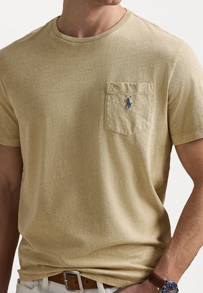 Τ-shirt κοντομάνικο, με λαιμόκοψη crewneck σε ανοιχτό μπεζ, με μπροστινή τσέπη που φέρει μπλε λογότυπο. Μαλακό ύφασμα με διακριτική υφή.