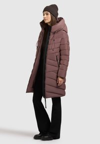Lang, polstret jakke i mauve med lodret quiltet design, hætte, justerbare snoretræk og lynlåslommer, parret med sorte bukser og støvler.