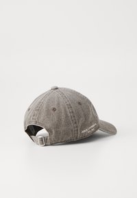 Gray cotton baseball cap with a textured finish, featuring a curved brim and adjustable fabric strap in the back. Logo stitched on the side.