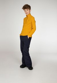 Pullover giallo a maniche lunghe con colletto a zip parziale, abbinato a pantaloni cargo blu navy con tasche laterali e scarpe nere.
