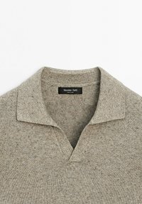 Hellbrauner Strickpullover mit weichem Kragen und V-Ausschnitt, der ein Massimo Dutti Markenetikett zeigt, das innen im Nacken eingenäht ist.