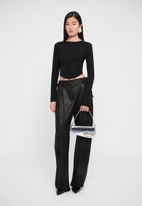 Black long-sleeve top with a fitted design, paired with loose black leather pants and a silver metallic handbag with a curved handle.
