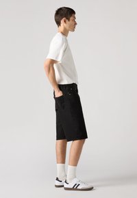 Črne jeans hlače s stranskimi žepi, kombinirane s preprosto belo majico in belimi supergami s črnimi črtami. Enostavno ozadje.