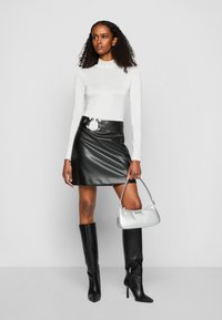 Langärmliges, hellgraues Oberteil; schwarzer Leder-Minirock mit Rundschnalle; kniehohe schwarze Stiefel; silberne Handtasche. Glatte Texturen überall.