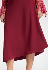 Vestido A-line burdeos con un dobladillo asimétrico, hecho de una tela suave. Las mangas tienen un vibrante patrón geométrico en rosa y naranja.