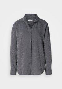 Camicia a righe bianca e nera, con taschino sul petto, colletto e maniche lunghe con polsini a righe contrastanti.
