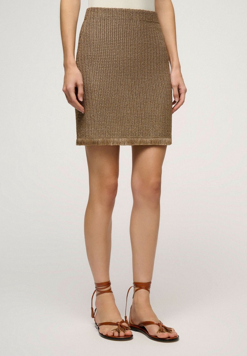 Jupe marron texturée longueur genoux avec ourlet à franges, portée avec des sandales plates en cuir marron clair à brides autour de la cheville.