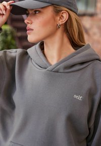 Szara bluza z kapturem, miękka w dotyku, z delikatnym haftem logo "self.". W połączeniu z dopasowaną czapką.